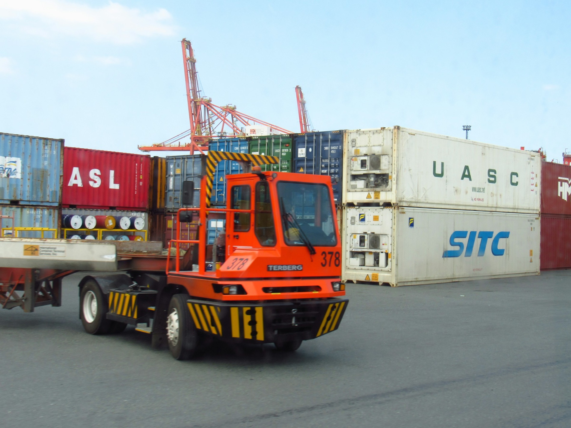 A terminal tractor moving a container chassis under ship to shore cranes at a marine terminal